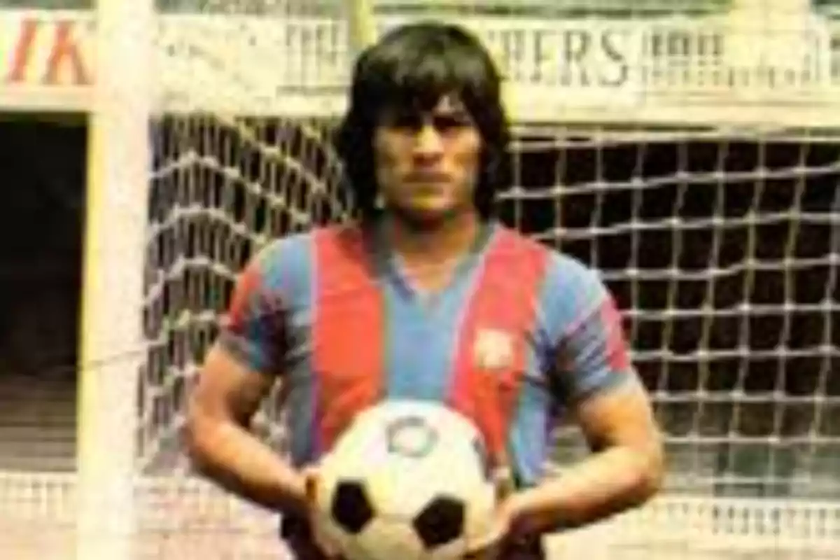 A soccer player in a blue and red uniform holds a ball in front of a goal. A soccer player in a blue and red uniform holds a ball in front of a goal.