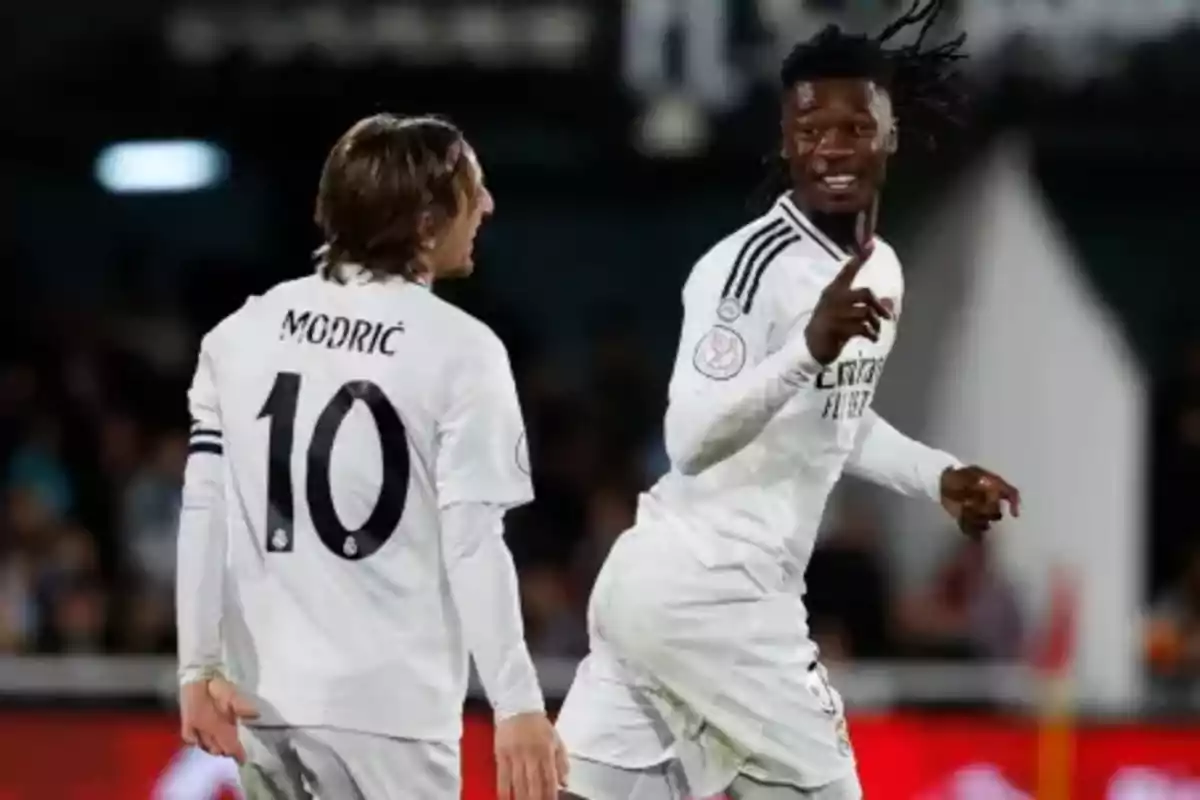 Two soccer players in white uniforms celebrate on the field during a match. Two soccer players in white uniforms celebrate on the field during a match.