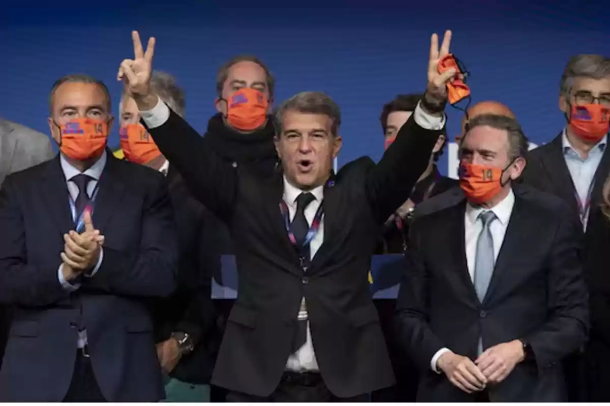 A group of people at an event, some wearing orange masks, while a man in the center raises his arms in a victory sign. A group of people at an event, some wearing orange masks, while a man in the center raises his arms in a victory sign.