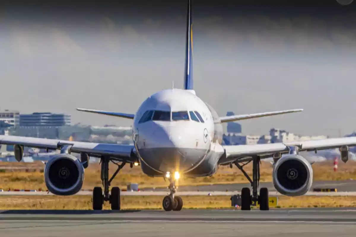 A commercial airplane on the runway of an airport, seen from the front, with buildings in the background.