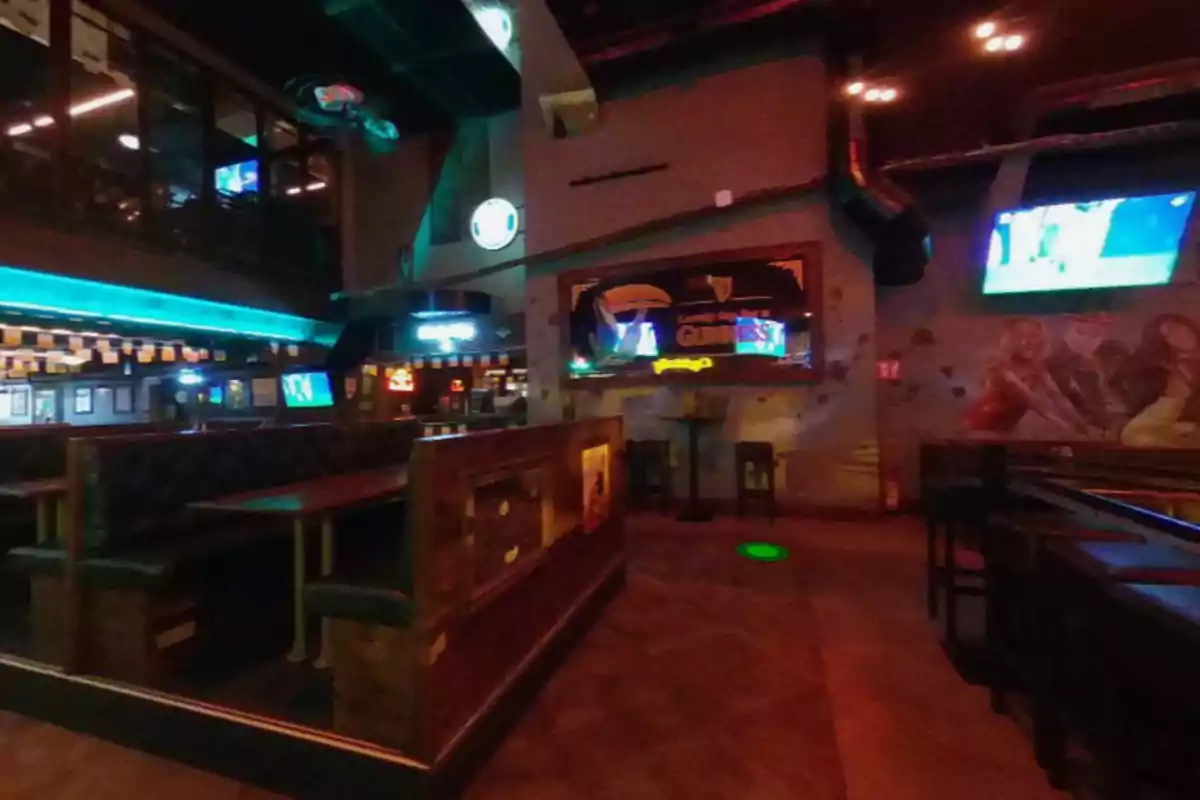 A bar with wooden tables, dim lighting, and television screens on the walls.