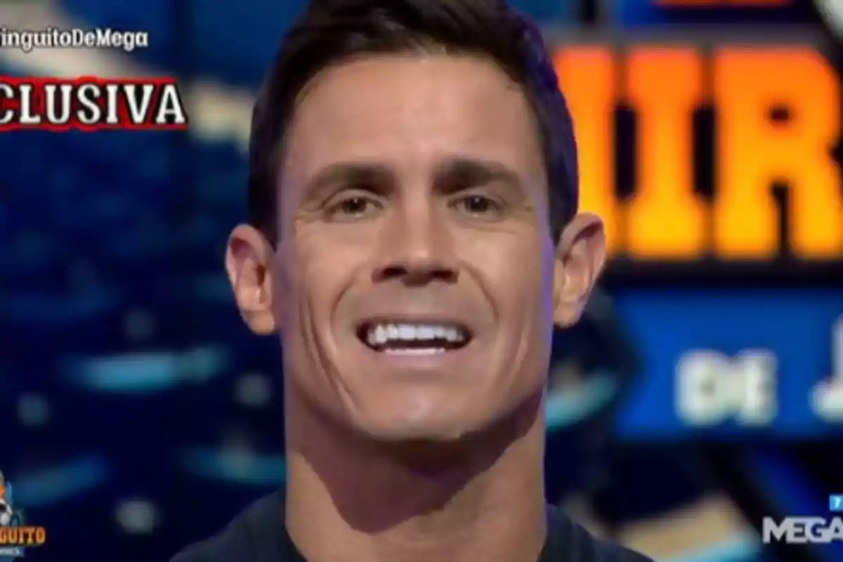 A smiling man on a television show with colorful graphics in the background.