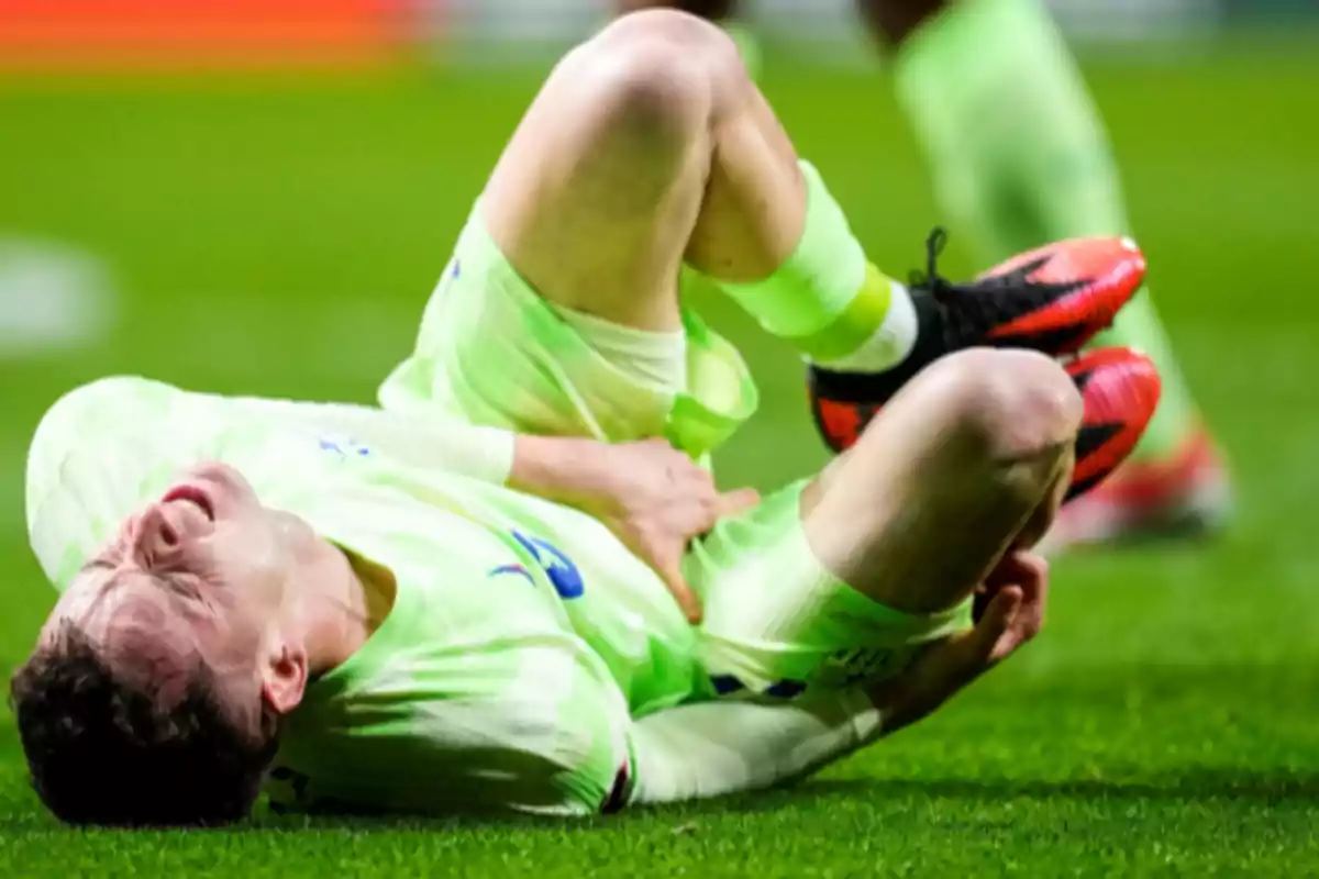 Soccer player on the ground with a pained expression, clutching his leg during a match.