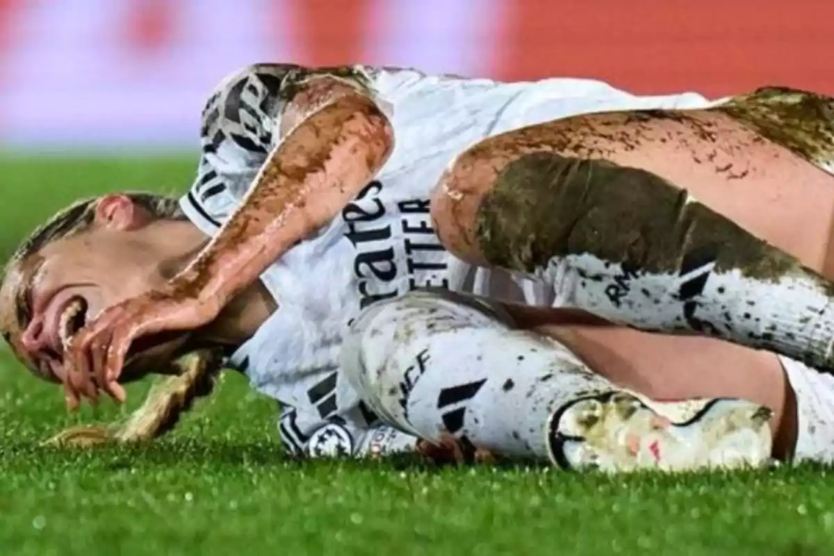 A player in a white uniform is on the ground covered in mud and appears to be in pain.