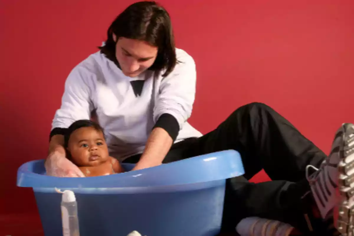 A person bathing a baby in a blue tub against a red background. A person bathing a baby in a blue tub against a red background.