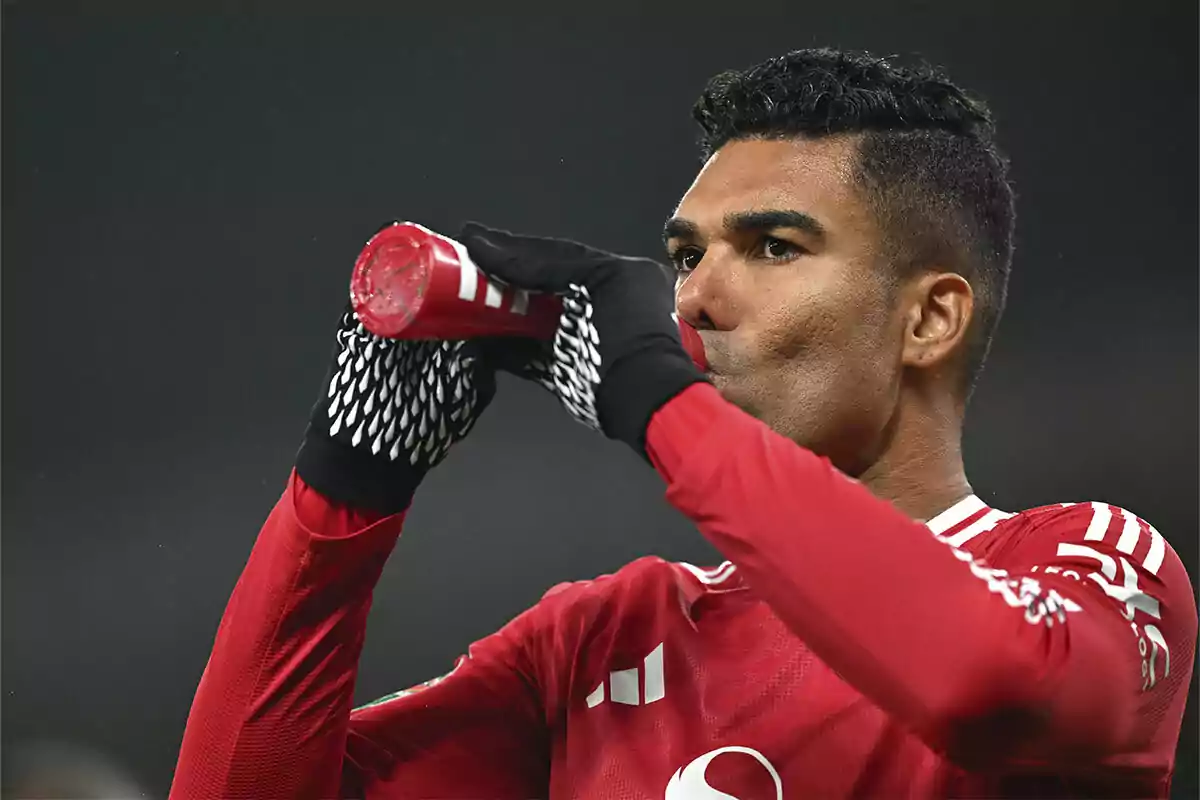 Casemiro in a red uniform and black gloves drinks from a bottle during a match.