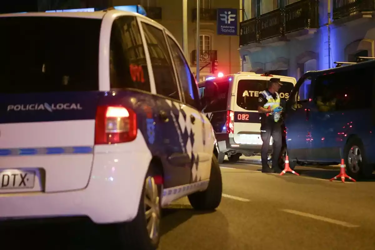 Una escena nocturna muestra a la policía local en una operación de control de tráfico con varios vehículos policiales y un agente interactuando con un conductor.