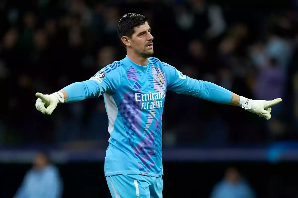 A soccer goalkeeper in a light blue uniform and white gloves stretches his arms in a stadium.