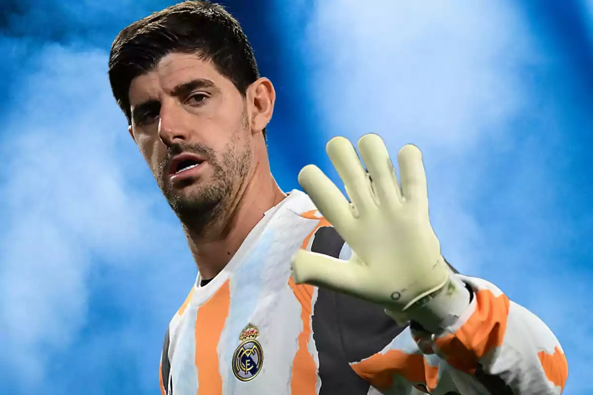 Un jugador de fútbol con uniforme de portero levantando la mano con guante en un fondo azul.