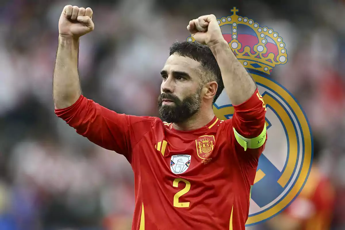 Dani Carvajal con uniforme rojo levantando los brazos en señal de victoria con el escudo del Real Madrid de fondo.