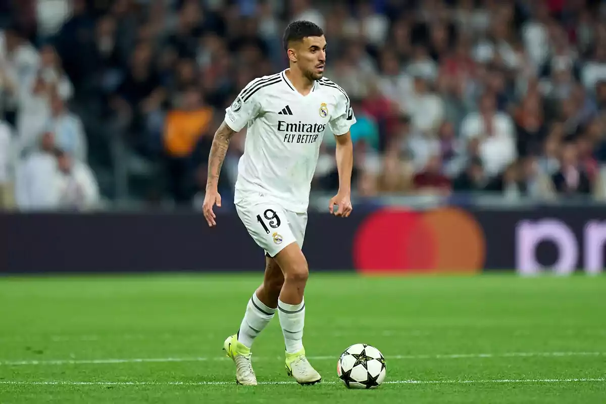 Un jugador de fútbol con el uniforme blanco del Real Madrid controla el balón en el campo durante un partido.