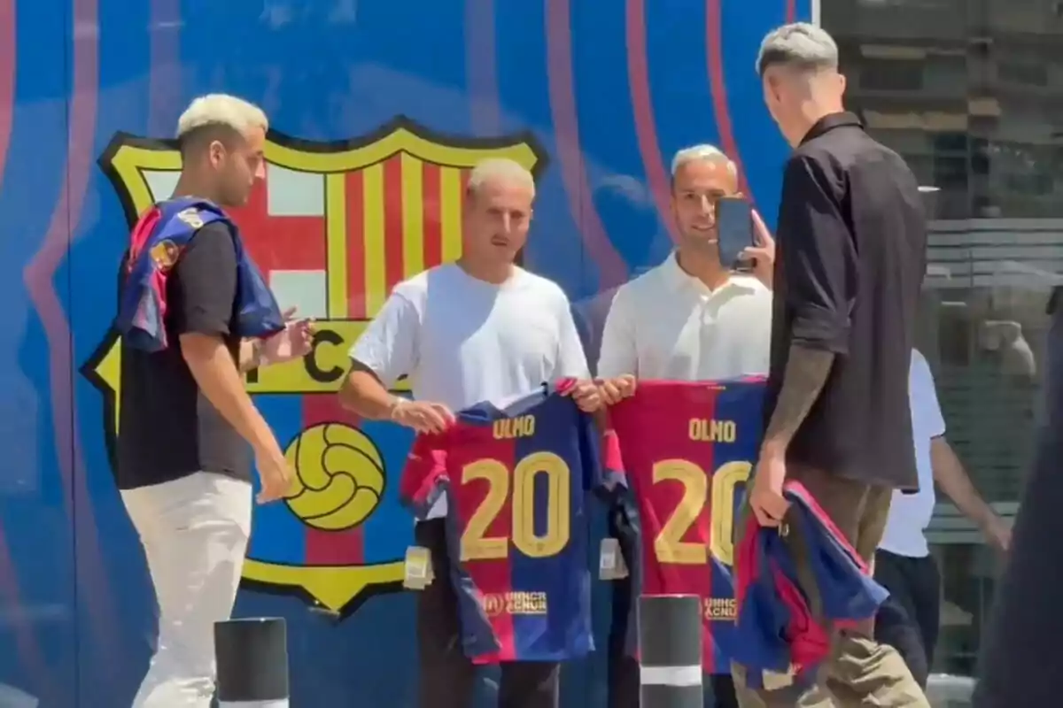 Un grupo de personas posa con camisetas del FC Barcelona con el número 20 y el nombre de Olmo frente a un mural del escudo del club.