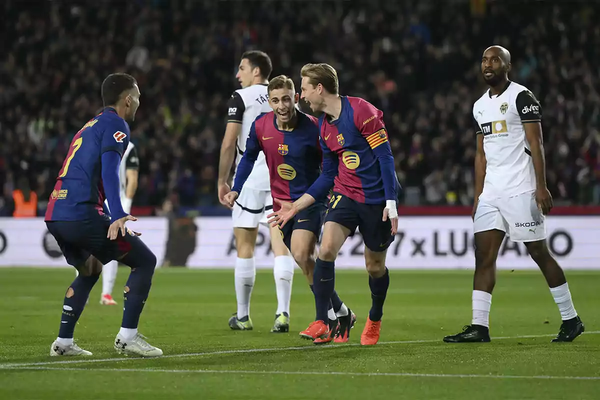 Football players celebrating a goal in a match between teams wearing blue and white uniforms.