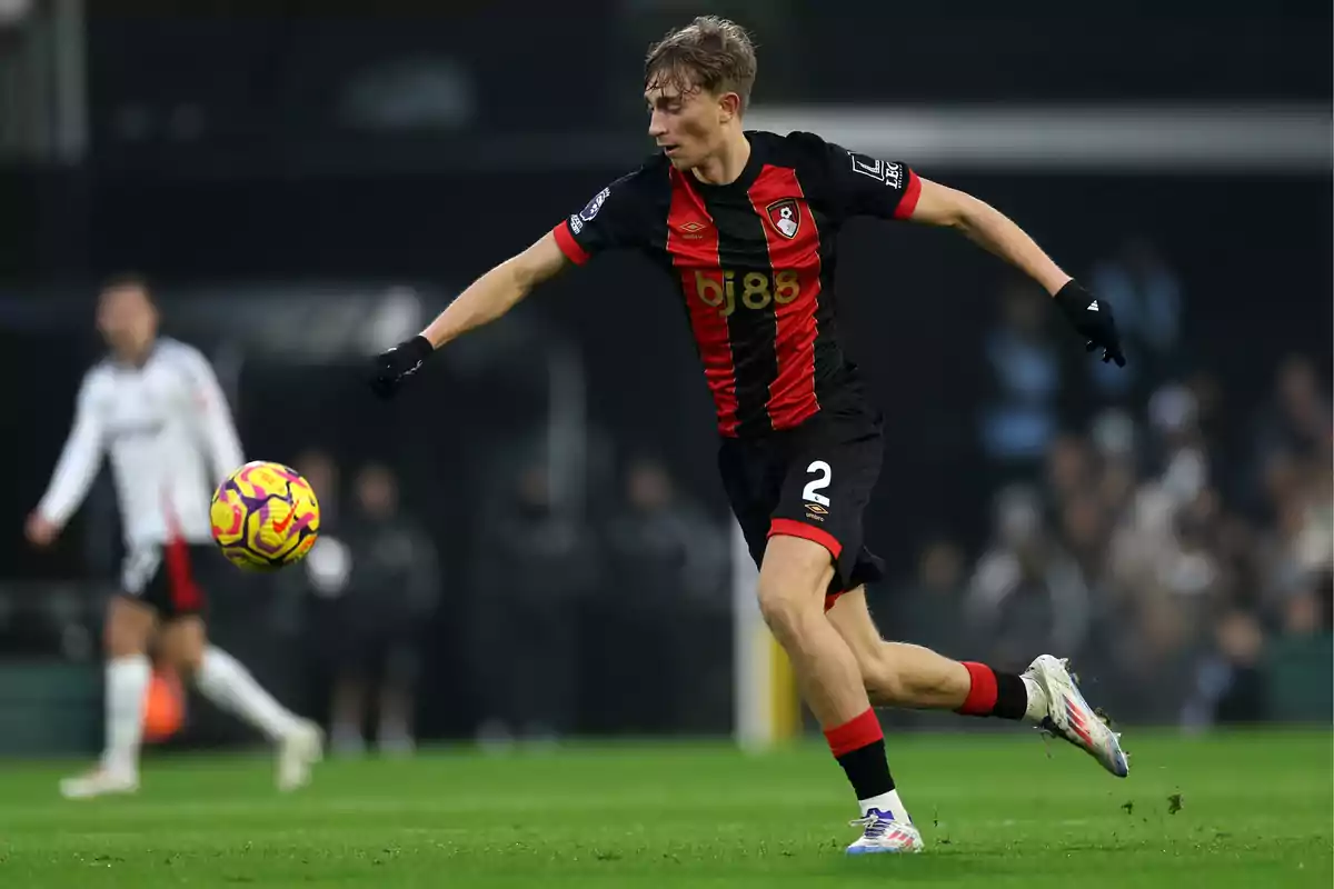 Soccer player in black and red uniform in action during a match, controlling the ball on the field.