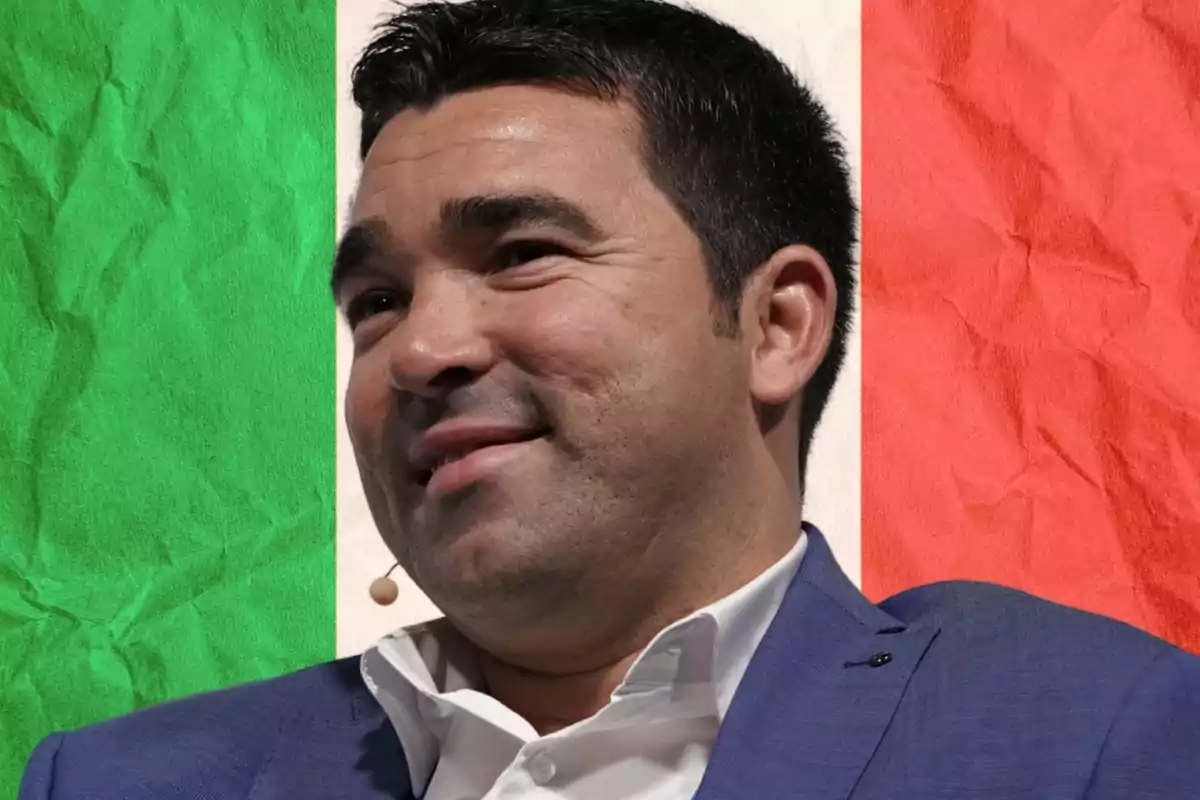Hombre de cabello oscuro con saco azul y camisa blanca, usando micrófono de diadema, frente a un fondo con los colores de la bandera de Italia