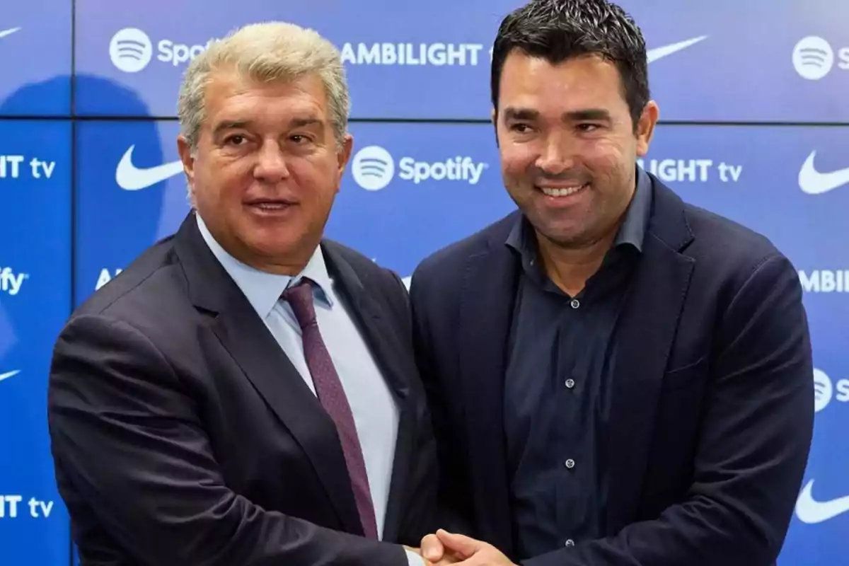 Dos hombres de traje se dan la mano frente a un fondo azul con logotipos de marcas.