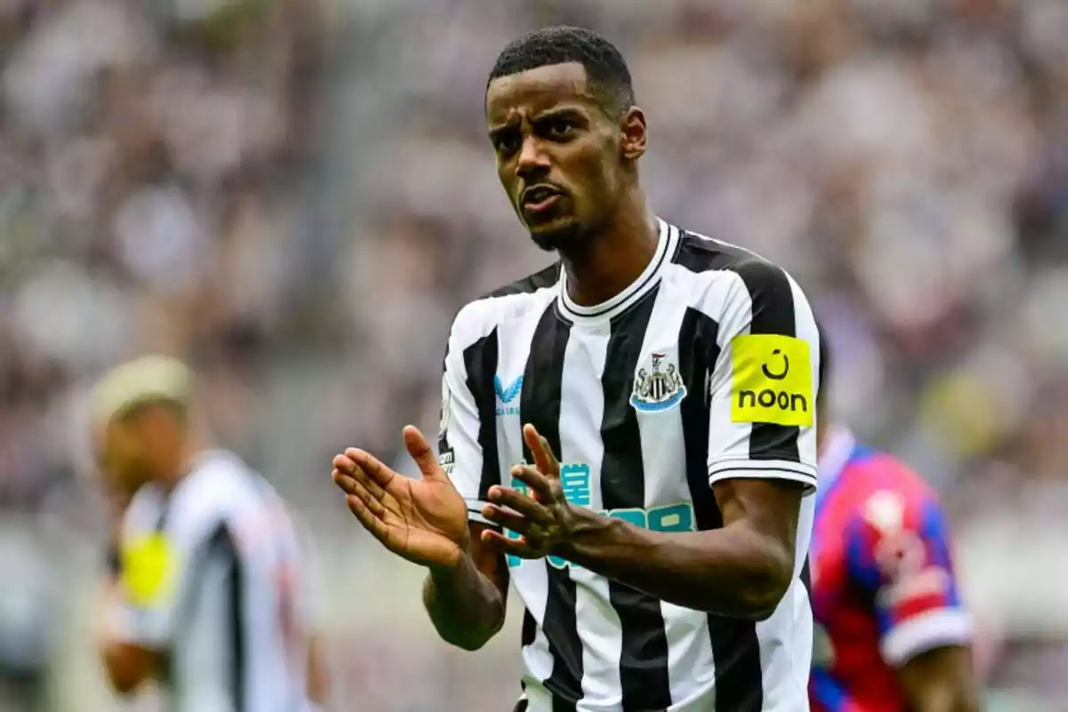 Jugador de fútbol con uniforme a rayas blancas y negras aplaudiendo en el campo durante un partido.