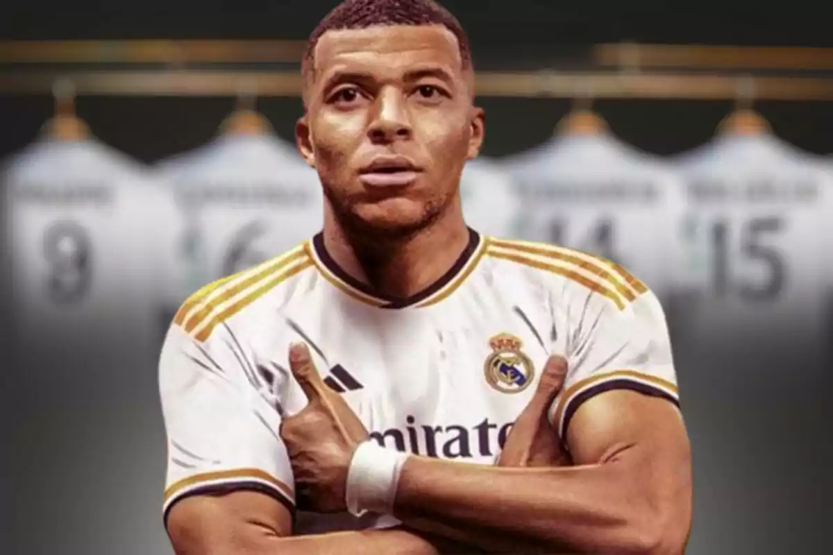 Mbappé con la camiseta del Real Madrid, con los brazos cruzados y varias camisetas colgadas en el fondo.