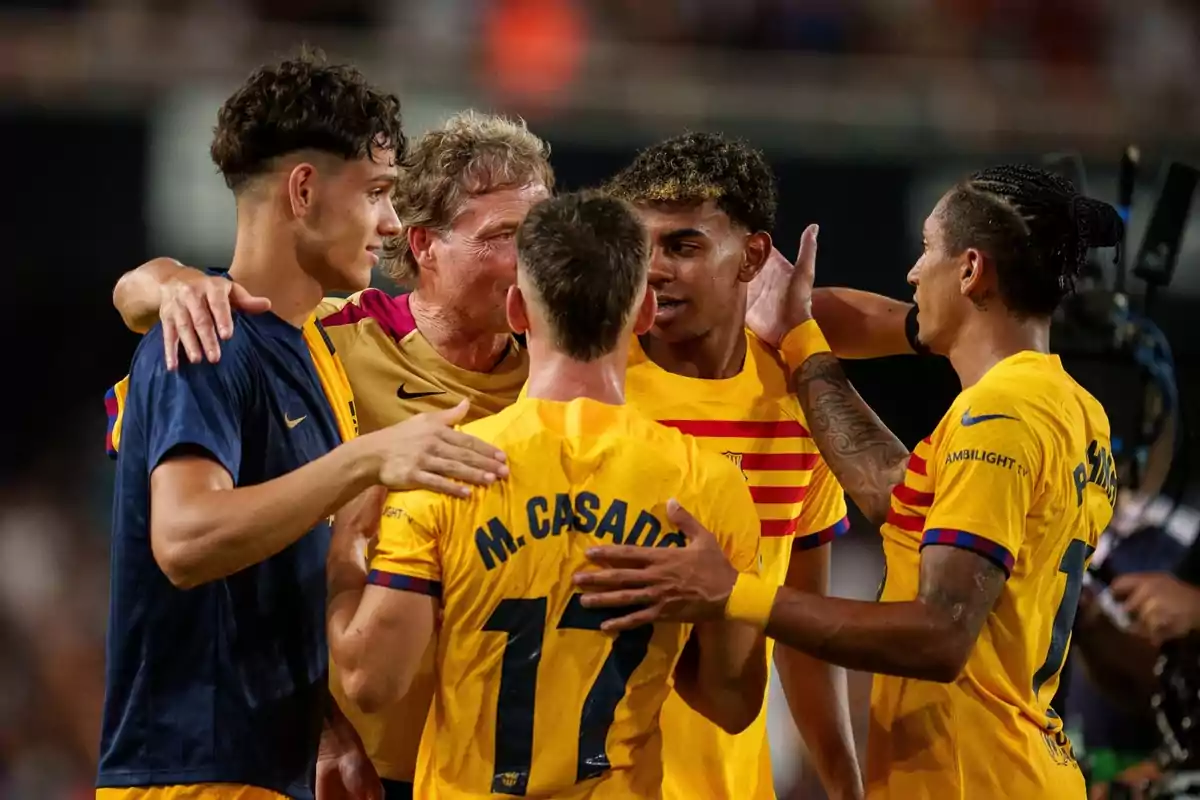 Football players celebrating together on the field, some in yellow shirts and one in a blue shirt.