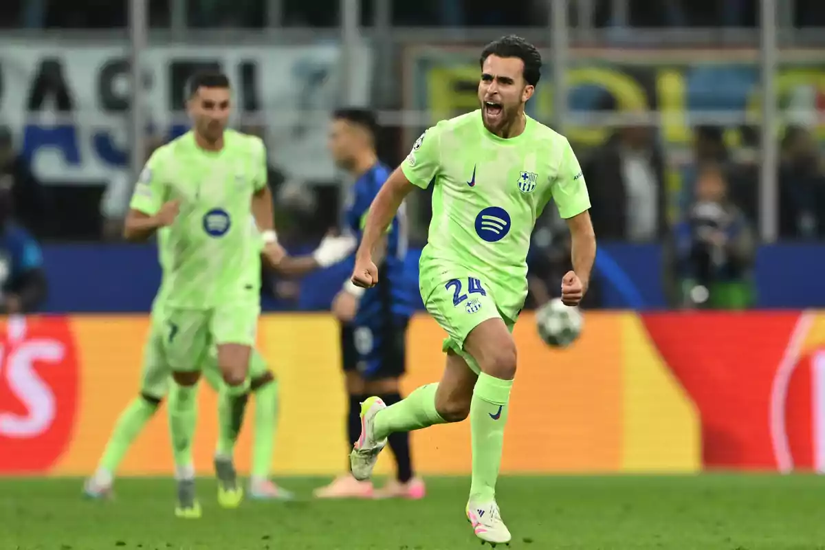 Un jugador de fútbol con uniforme verde celebra en el campo durante un partido, con otros jugadores y público de fondo. Un jugador de fútbol con uniforme verde celebra en el campo durante un partido, con otros jugadores y público de fondo.