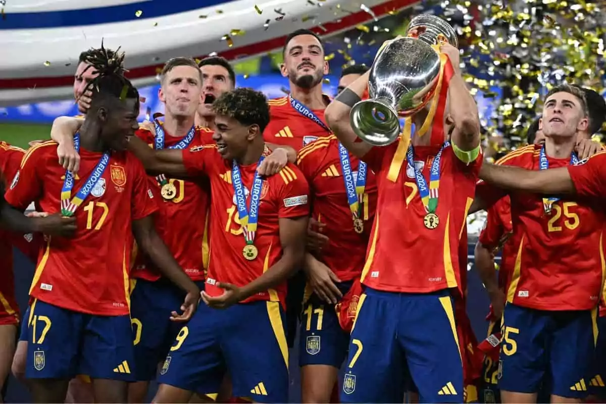 Jugadores de la selección española de fútbol celebrando con el trofeo de la Eurocopa 2021, vistiendo uniformes rojos y medallas alrededor del cuello.