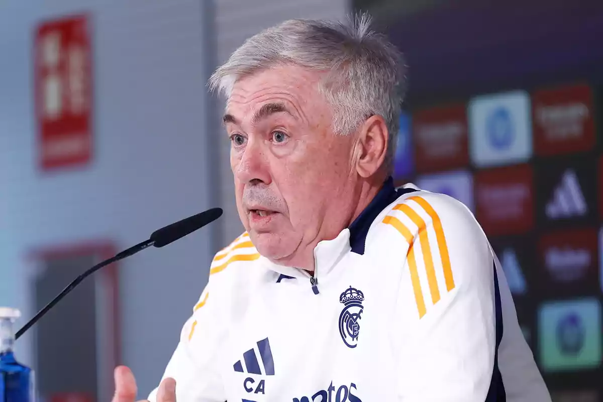 Un hombre con uniforme deportivo blanco y amarillo hablando en una conferencia de prensa.