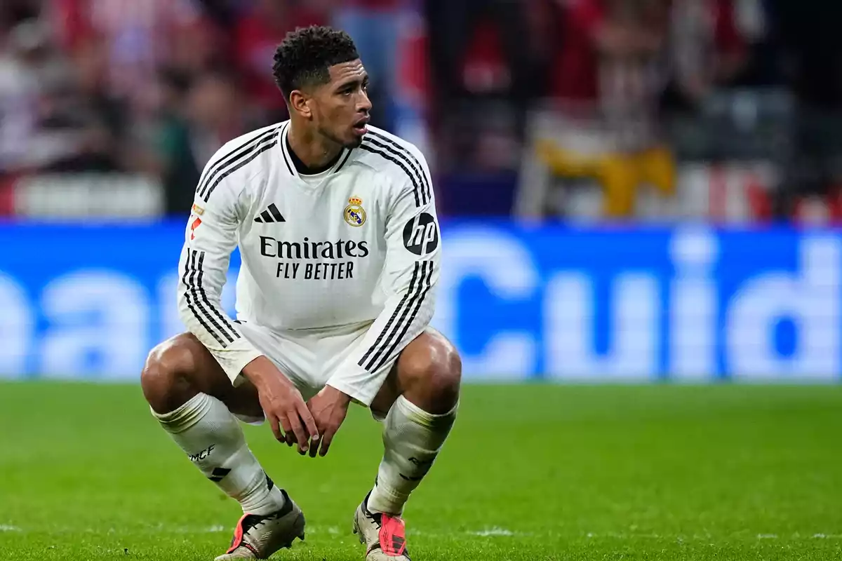 A Real Madrid soccer player, dressed in the team's white uniform, crouches on the field during a match.