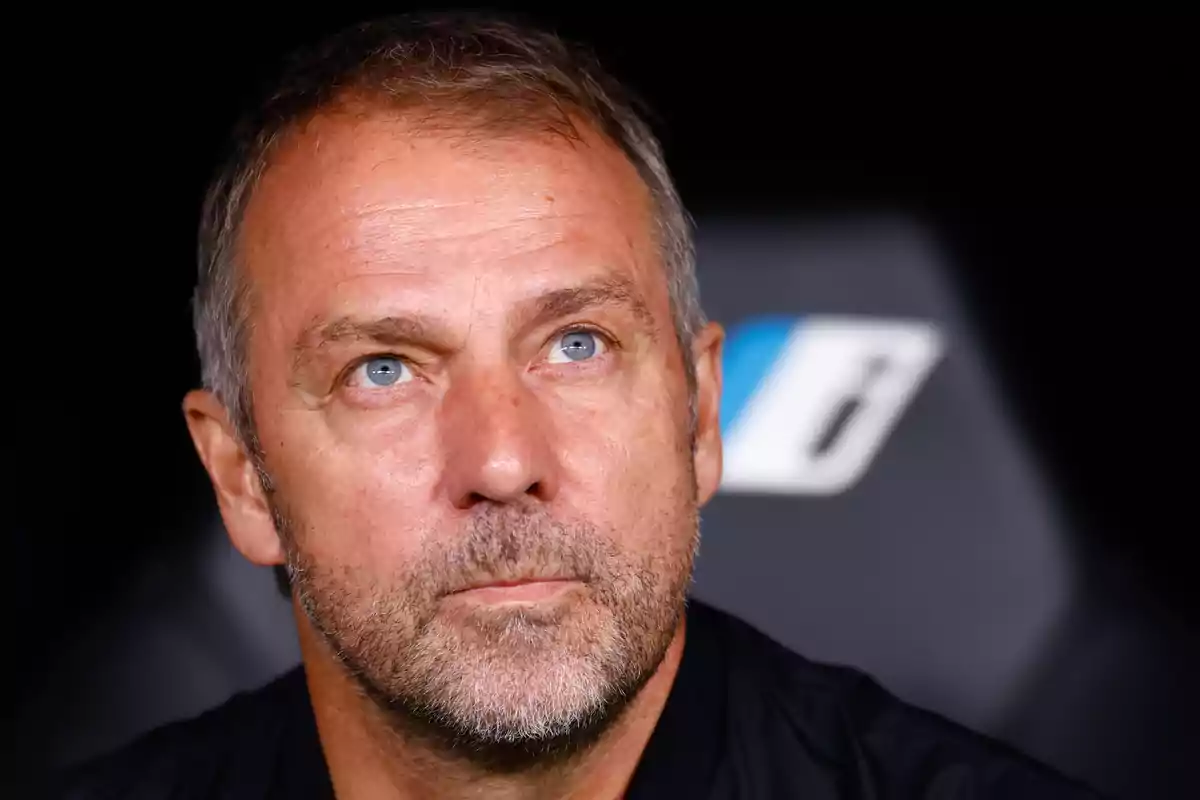 A middle-aged man with a beard and short hair looks up thoughtfully against a dark background.