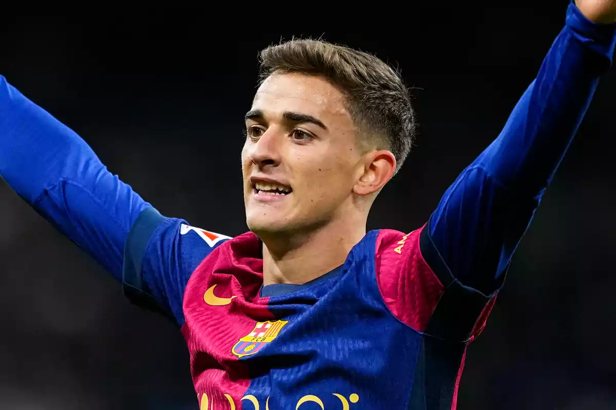 A soccer player in a blue and red uniform raises his arms in celebration.