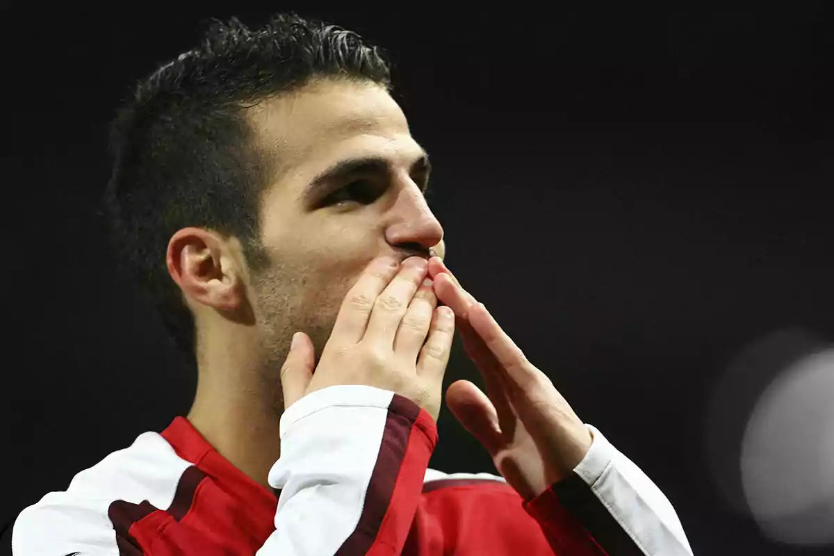 Cesc Fàbregas con uniforme rojo y blanco del Arsenal da un beso con ambas manos.