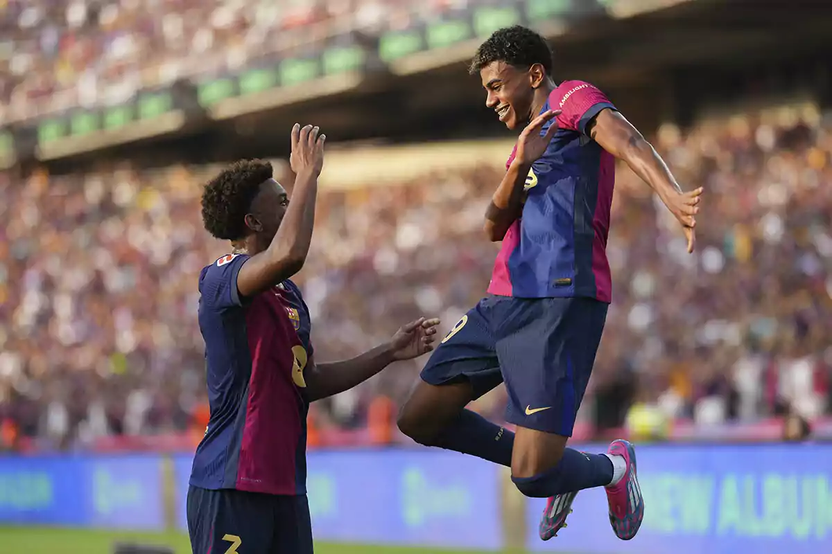 Lamine Yamal y Balde celebran un gol en un estadio lleno de espectadores, uno de ellos saltando en el aire mientras el otro levanta la mano para chocar los cinco.