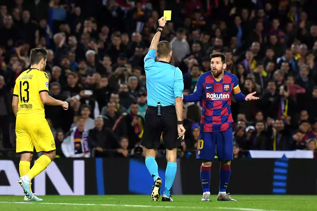 A referee shows a yellow card to a Barcelona player while another Dortmund player walks away in a soccer match. A referee shows a yellow card to a Barcelona player while another Dortmund player walks away in a soccer match.