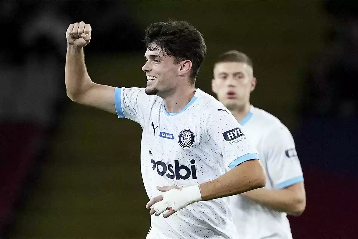 Miguel Gutiérrez celebrando un gol con el puño en alto y una sonrisa, vistiendo un uniforme blanco con detalles azules.