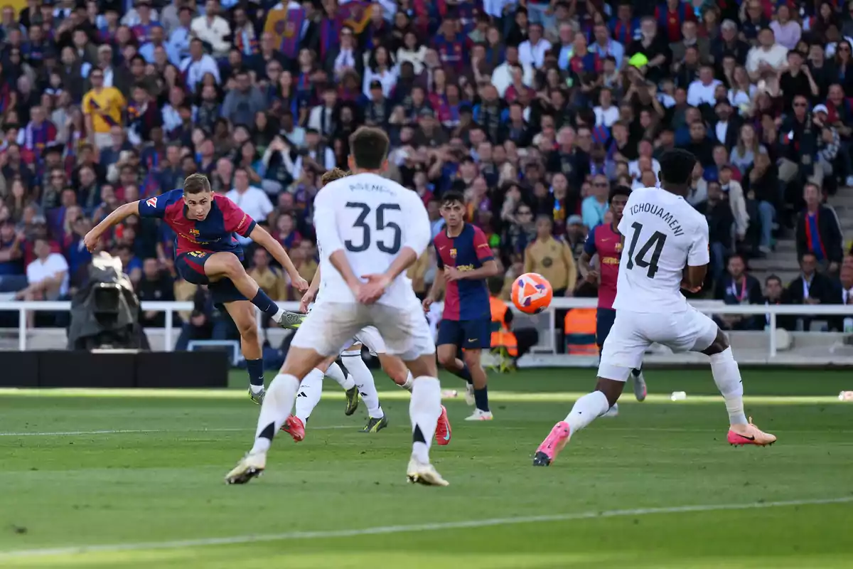 A player in a blue and red uniform kicks the ball while other players in white uniforms try to block him in a stadium full of spectators. A player in a blue and red uniform kicks the ball while other players in white uniforms try to block him in a stadium full of spectators.