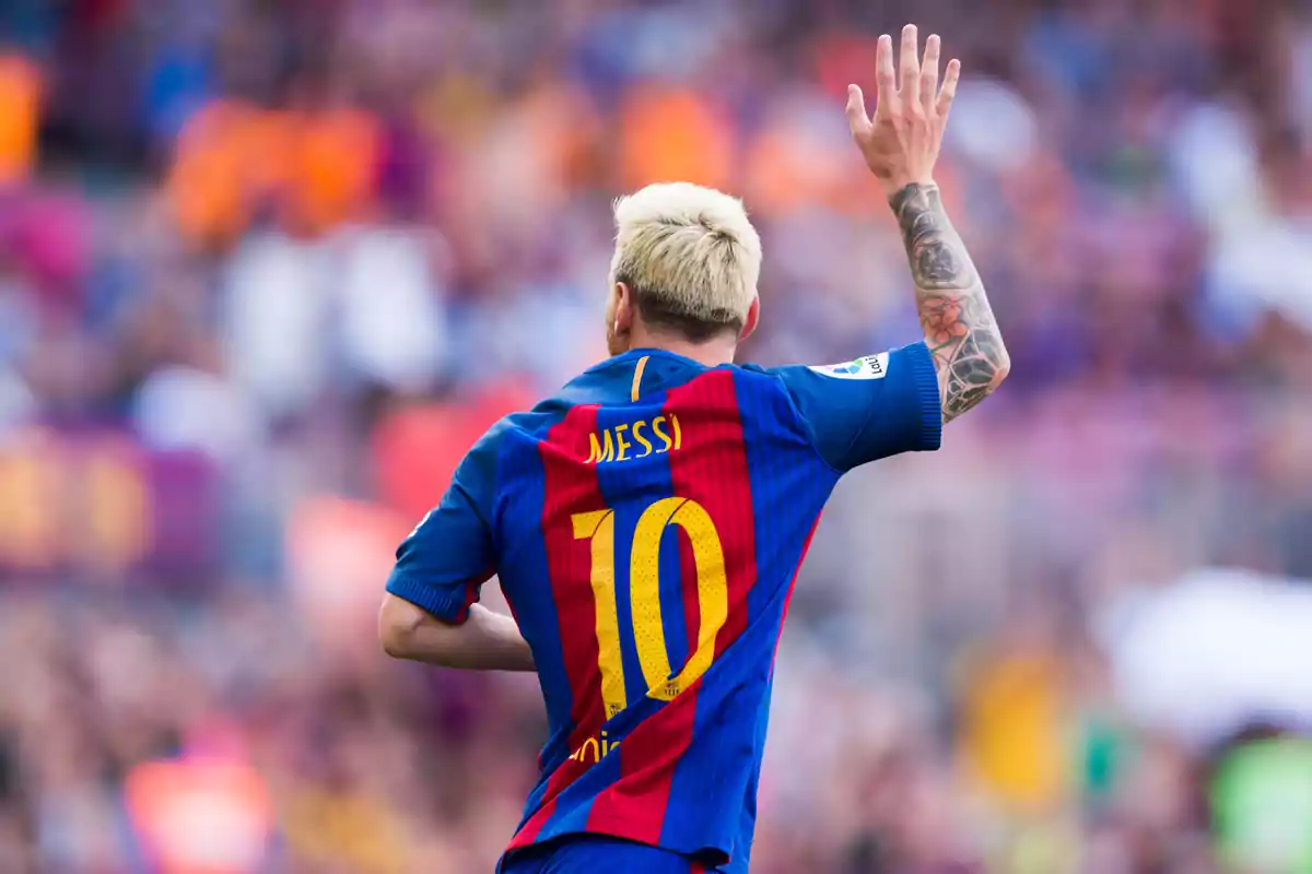 Soccer player in blue and red jersey number 10 raising his hand in a stadium full of spectators.