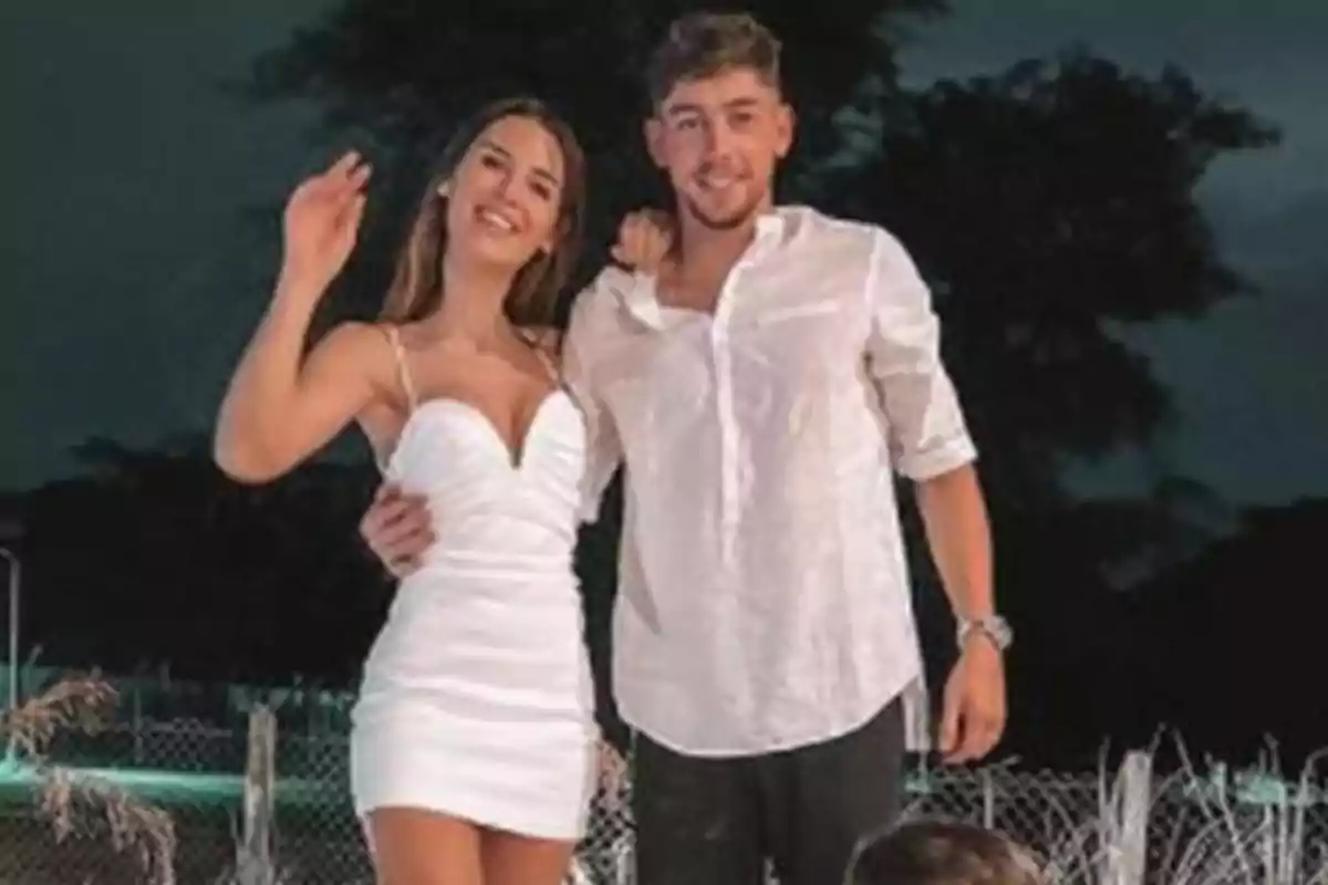 A young couple smiles and poses for the camera outdoors at night.