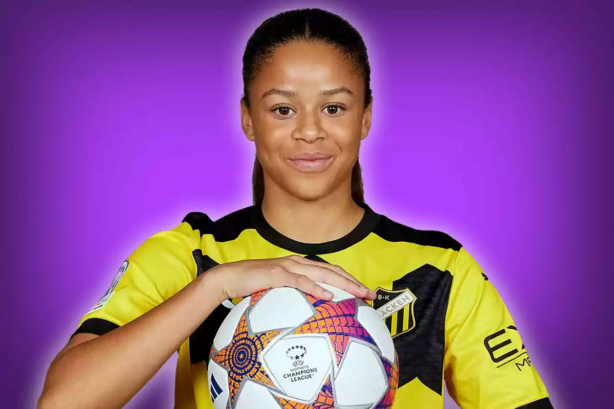 Futbolista con uniforme amarillo y negro sosteniendo un balón de la Champions League sobre un fondo morado