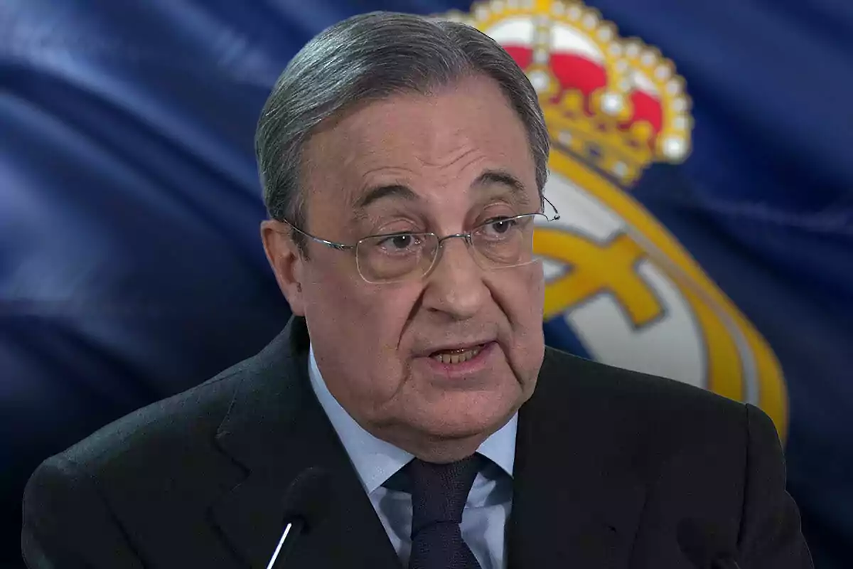 Florentino Pérez con gafas y traje oscuro hablando frente a un micrófono con un fondo que muestra una bandera del Real Madrid.