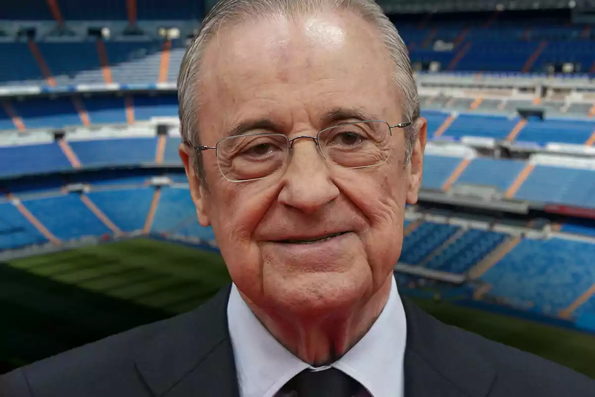 Florentino Pérez con gafas y traje oscuro sonríe en un estadio de fútbol vacío.