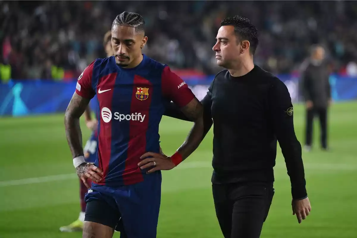 Un jugador de fútbol del FC Barcelona con el uniforme del equipo es acompañado por un hombre en un campo de fútbol. Un jugador de fútbol del FC Barcelona con el uniforme del equipo es acompañado por un hombre en un campo de fútbol.
