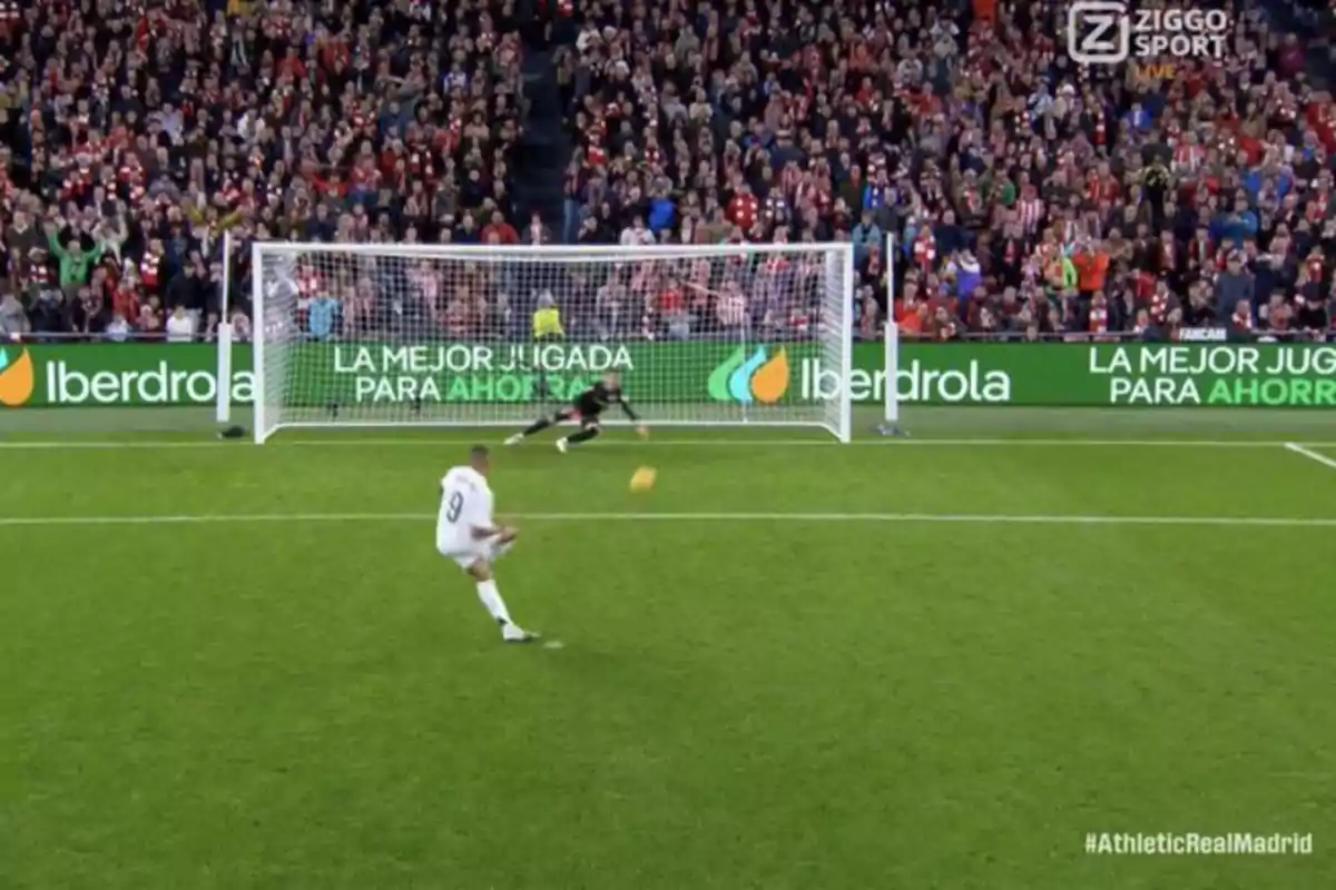 Football player in the act of kicking a penalty while the goalkeeper dives to try to stop the ball, with a crowd of spectators in the background. Football player in the act of kicking a penalty while the goalkeeper dives to try to stop the ball, with a crowd of spectators in the background.