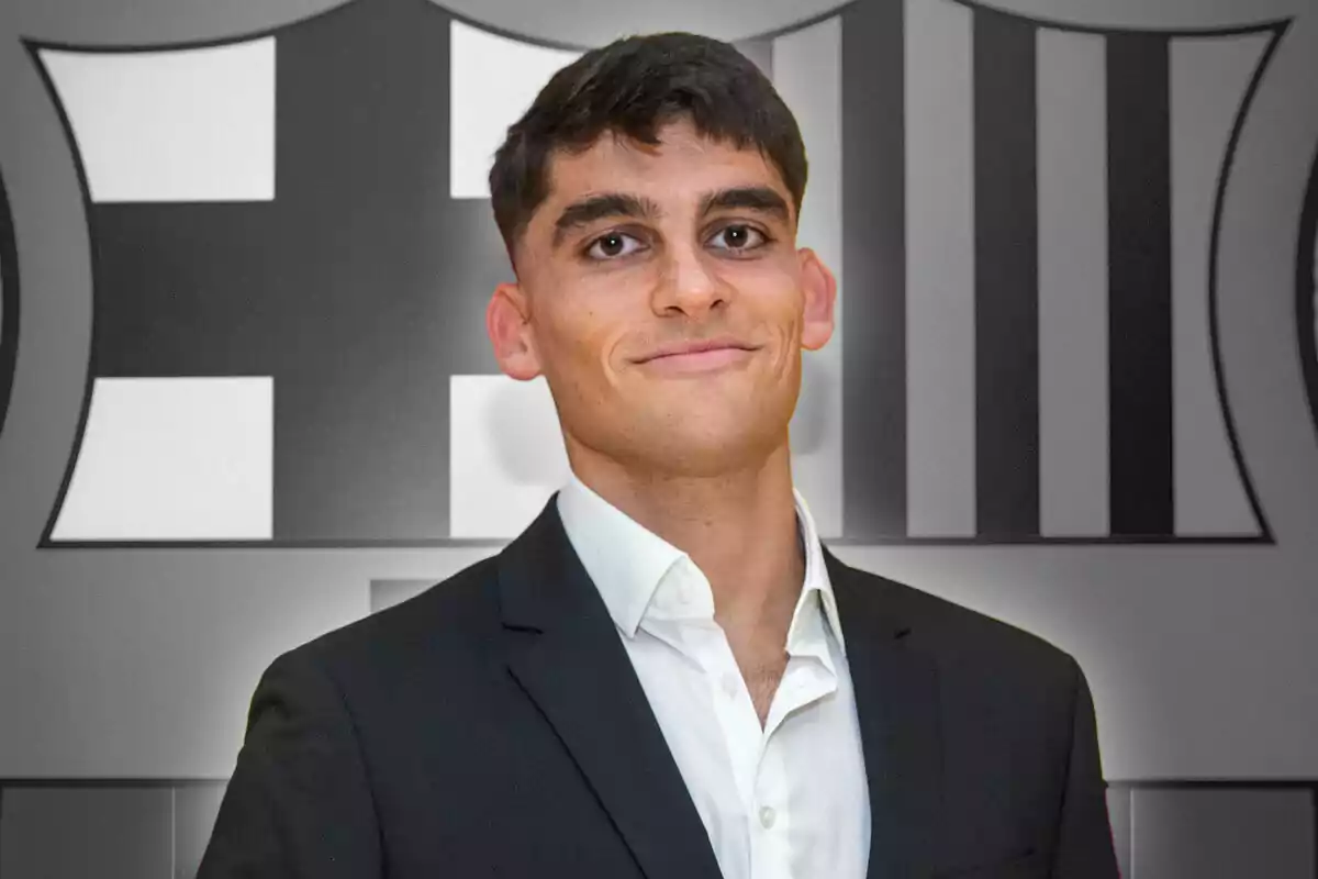 A young man in a dark suit and white jersey smiles in front of a background with black and white geometric patterns.