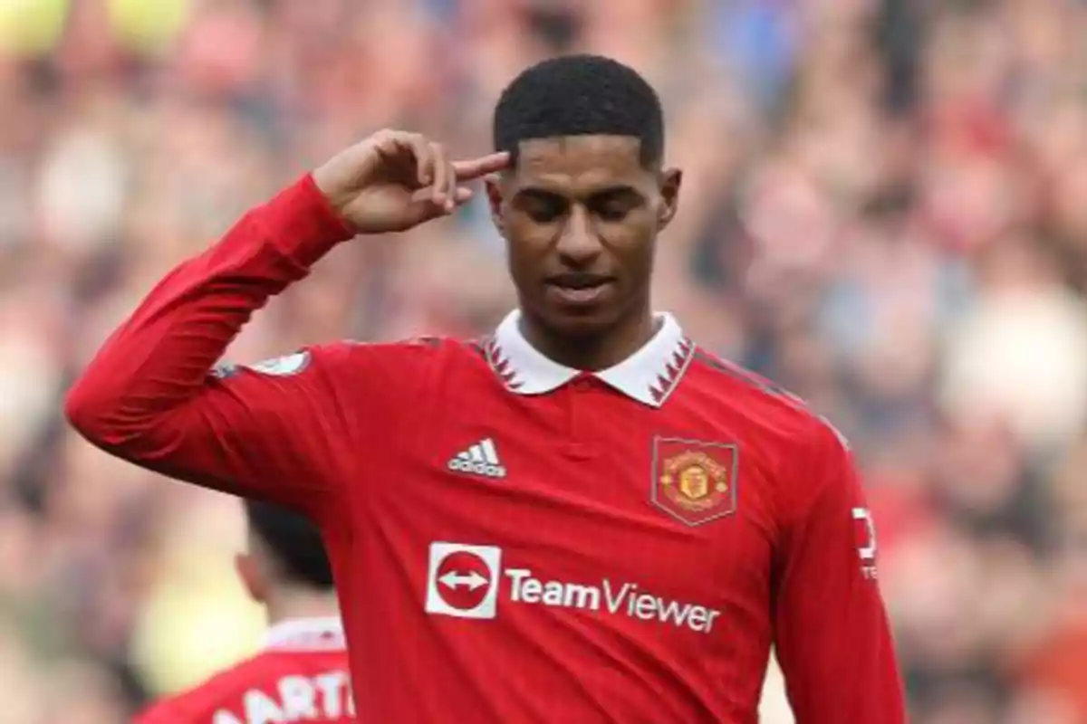 Jugador de fútbol con uniforme rojo del Manchester United haciendo un gesto con la mano en la frente durante un partido.