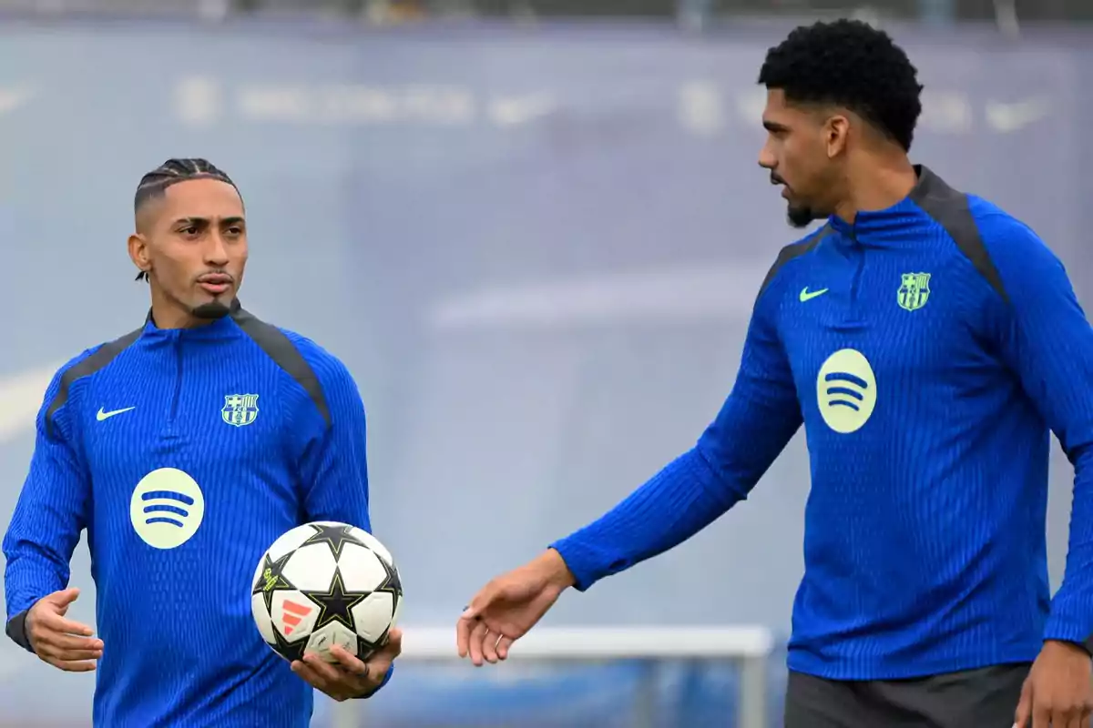 Two players in blue training uniforms talk while one holds a ball.