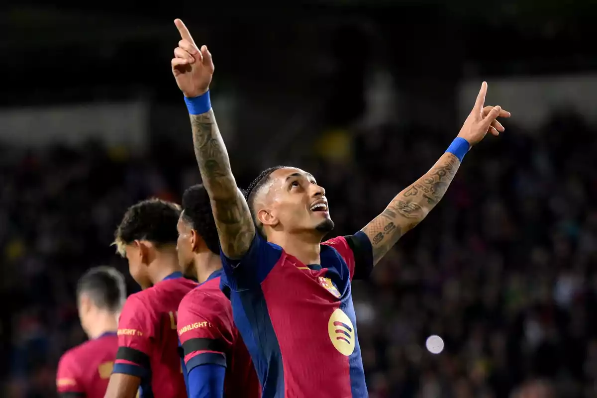 A player in a blue and maroon uniform raises his arms in celebration in a stadium full of spectators.