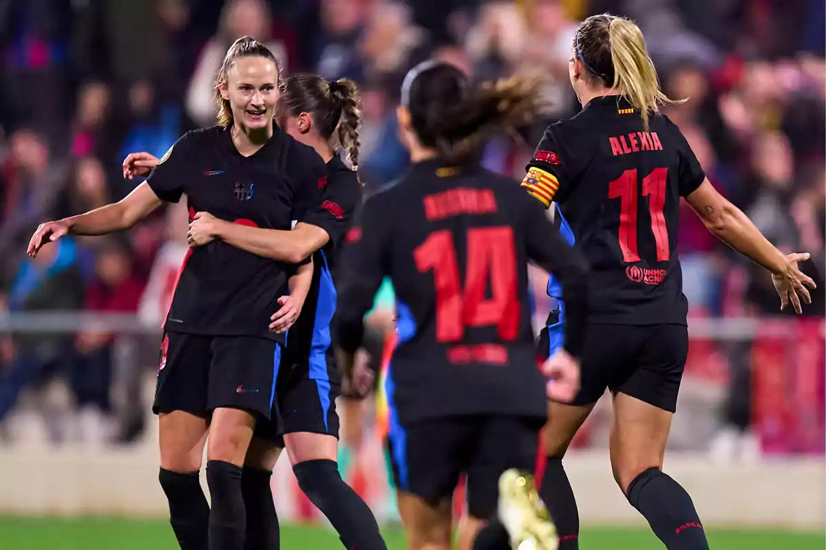 Female soccer players celebrating a goal on the field in black uniforms with red details. Female soccer players celebrating a goal on the field in black uniforms with red details.