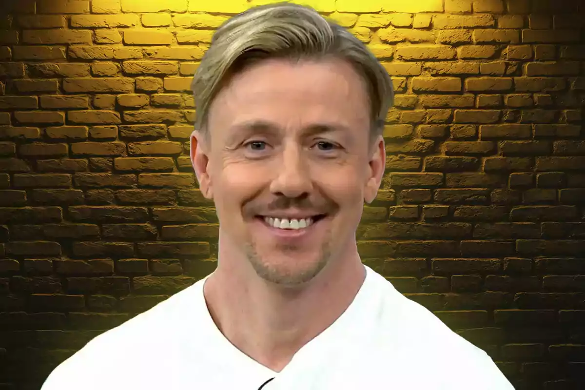 Blond man smiling in front of a brick wall lit with yellow light