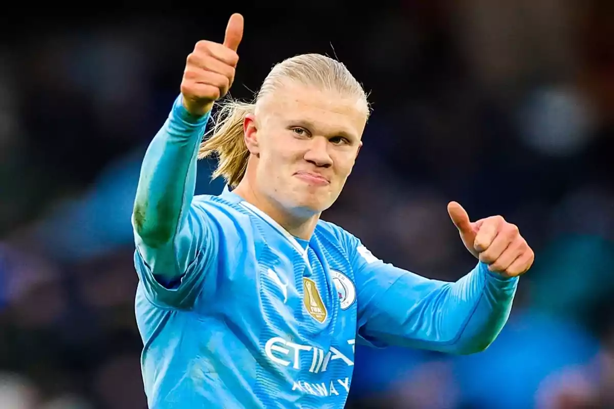 A soccer player in a blue uniform raises both thumbs in approval.