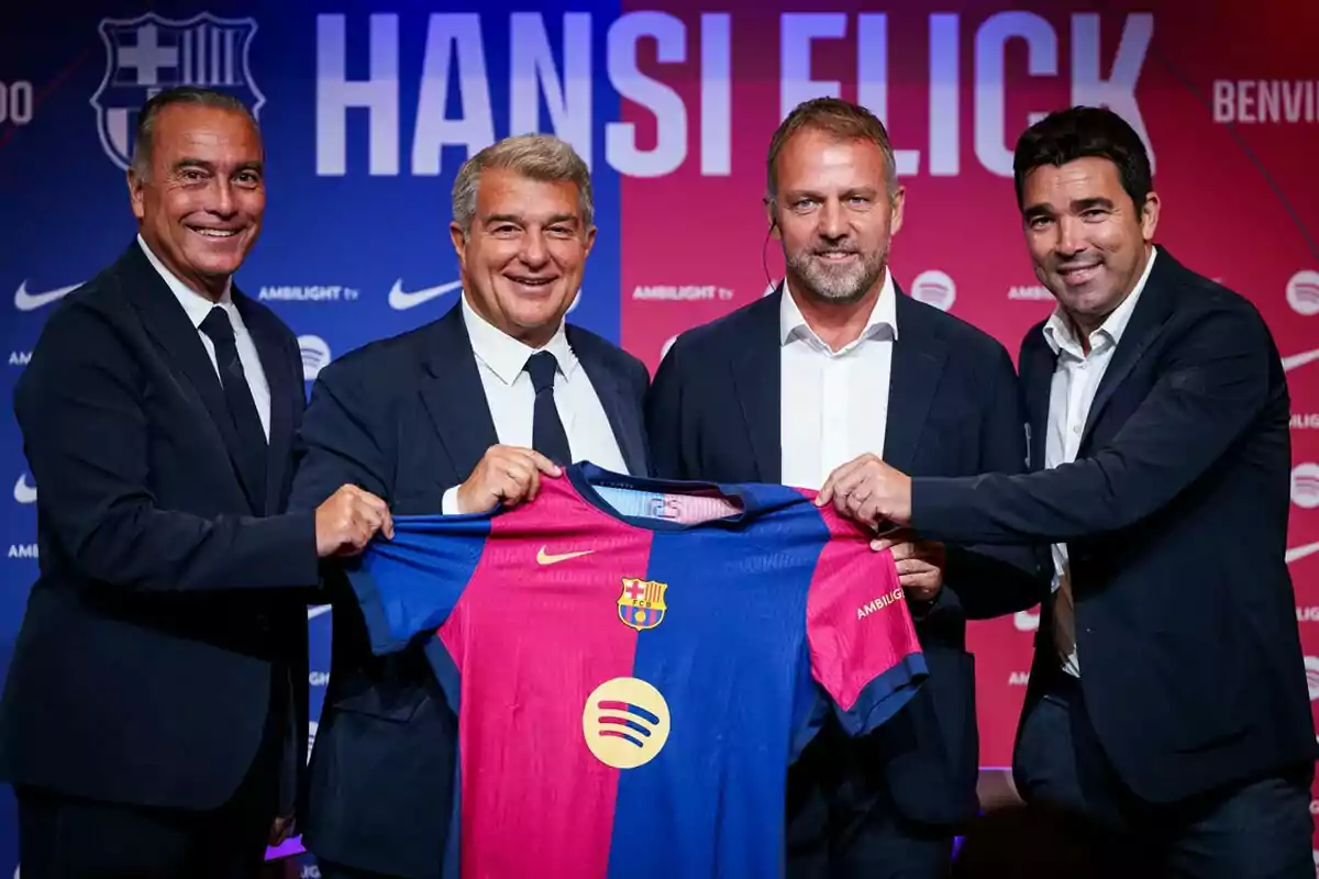 Rafa Yuste, Laporta, Hansi Flick y Deco, en trajes, sostienen una camiseta del FC Barcelona en un evento de bienvenida.