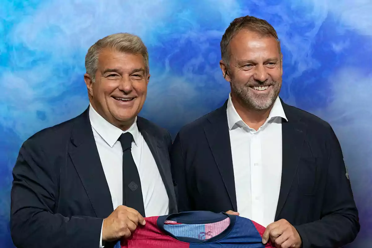 Laporta y Flick sonrientes, vestidos con trajes oscuros y corbatas, sostienen una camiseta de fútbol azul y roja frente a un fondo azul.